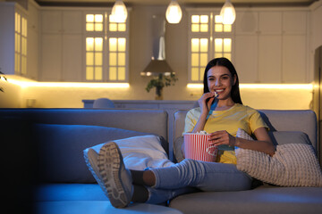 Obraz premium Young woman watching movie with popcorn on sofa at night, space for text