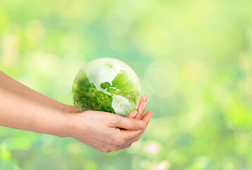 Hand holding globe glass world ball with green grass field in side the globe glass on nature blur background. eco concept