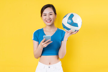 Beautiful Asian woman posing with soccer ball on blue background