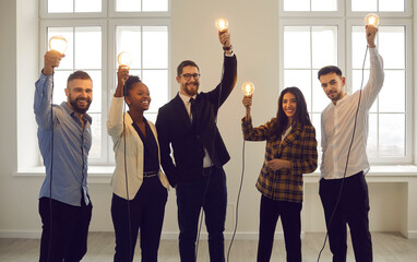 Creative team of international business people stands in the office with raised light bulbs that...