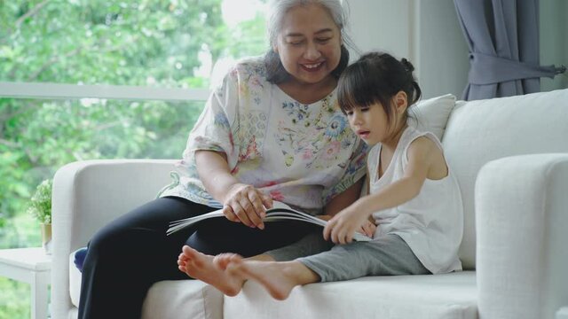 Senior lifestyle concept : A kind and gentle Asia grandmother teaching her granddaughter to read write and drawing on a white board at home