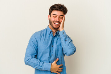 Young caucasian man isolated on white background laughs happily and has fun keeping hands on stomach.