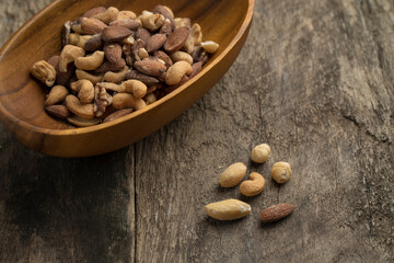 Salted mixed nuts in wooden bowl on textured wooden table.