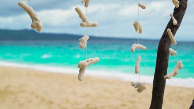 White sea shells on suspension with the sandy beach sea ocean background. Sea shells on the rope. Decorations made from white sea shells. Shallow focus. Travel concept.