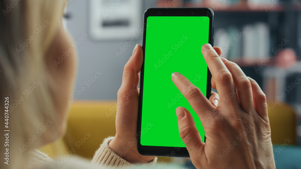 Poster Beautiful Authentic Female Using a Smartphone with Green Screen Mock Up Display at Home Living Room while Lying on a Couch Sofa. She's Browsing the Internet and Checking Videos on Social Networks.