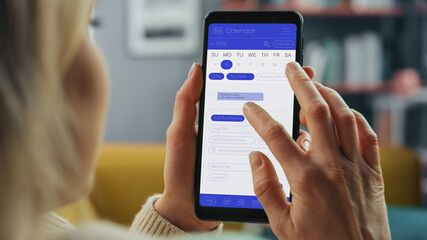 Beautiful Authentic Female Using a Smartphone with Calendar Application at Home Living Room while Lying on a Couch Sofa. She's Making Plans and Checking Event Schedule for a Day.