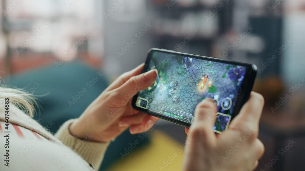 Poster close up on hands playing an rpg strategy video game on a horizontally held smartphone at home livin