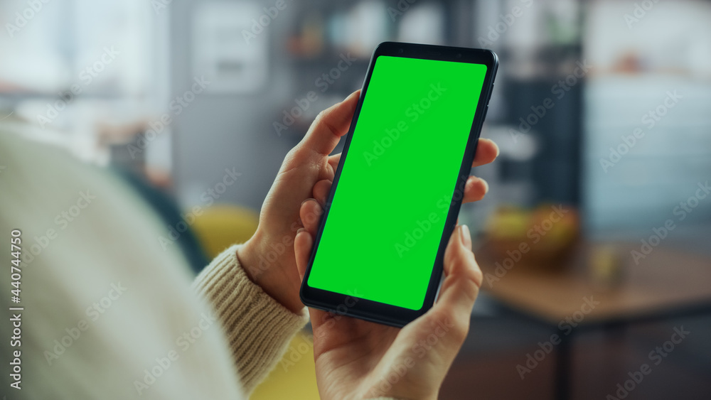 Aufkleber Close Up of an Authentic Female Using Smartphone with Green Screen Mock Up Display at Home Living Room while Lying on a Couch Sofa. She's Browsing the Internet and Checking Videos on Social Networks.