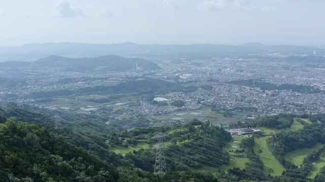 Looking down from hadano mountains to the nearby city. Breath-taking drone shot of nature and urban settlement.