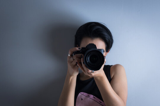 chica alternativa de pelo corto fotografa hace foto con camara profesional sobre un fondo neutro 