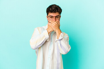 Young caucasian man isolated on blue background covering mouth with hands looking worried.