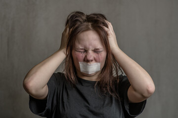 Tear-stained unhappy teen girl with a taped mouth trying scream