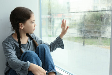 Sad little girl near window indoors on rainy day