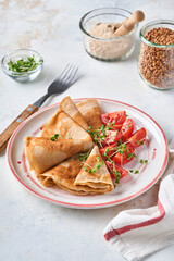 Stack of gluten free buckwheat flour crepes pancakes with cherry tomatoes and arugula microgreens on white plate, homemade healthy baking for breakfast. Mock up. Copy space.