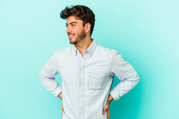 Young caucasian man isolated on blue background confident keeping hands on hips.