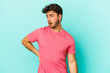 Young caucasian man isolated on blue background suffering a back pain.