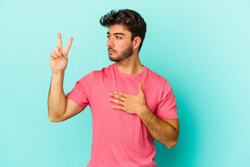 Fototapeta premium Young caucasian man isolated on blue background taking an oath, putting hand on chest.