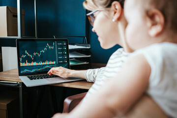 Handsome woman with her cute baby investing in world stock market, using her laptop and online...