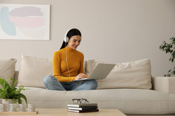 Woman with laptop and headphones sitting on sofa at home