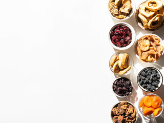 Obraz na płótnie Canvas Flat lay various dried fruits and berries in bowls on white background with shadows. Vegan healthy natural snacks.