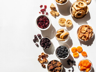 Flat lay various dried fruits and berries in bowls on white background with shadows. Vegan healthy natural snacks.