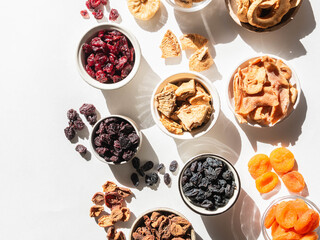 Flat lay various dried fruits and berries in bowls on white background with shadows. Vegan healthy natural snacks.