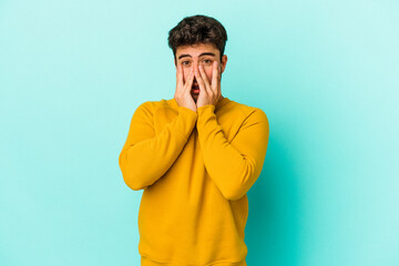 Young caucasian man isolated on blue background shocked, covering mouth with hands, anxious to discover something new.