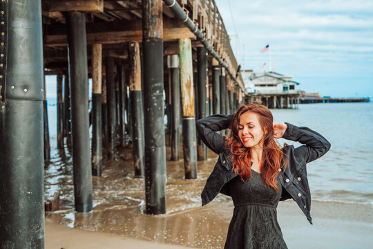 Beautiful young woman with long hair stands near the pier on the beach in Santa Barbara, California, USA