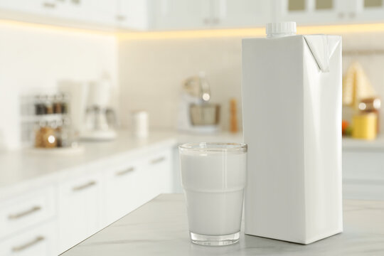 Carton box and glass of milk on table in kitchen, space for text
