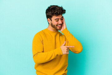 Young caucasian man isolated on blue background saying a gossip, pointing to side reporting something.