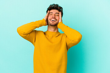 Naklejka premium Young caucasian man isolated on blue background laughs joyfully keeping hands on head. Happiness concept.
