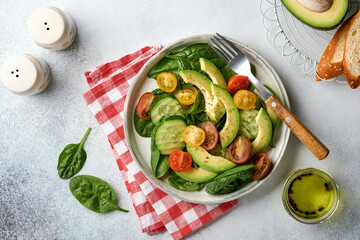 Fototapeta na wymiar Avocado, red, yellow, black cherry tomato, spinach and cucumber fresh salad with spices pepper and olive oil in grey bowl on grey slate, stone or concrete background. Healthy food concept. Top view.