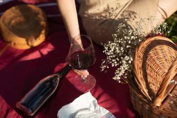 Outdoor picnic in summer sunny day. The red wine glass in a woman's hand. 