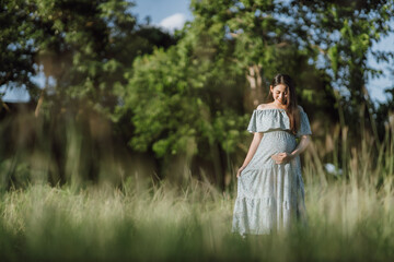 Asian young pregnant woman in blue dress relaxing and enjoying life in grass nature at summer day. Healthy pregnant. Copy space