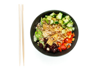 Vegetarian poke bowl in design black bowl with chopsticks below, isolated on white background. Green cucumber, red pepper, peanuts, corn, beetroot on top of sushi rice. Healthy vegetarian food.