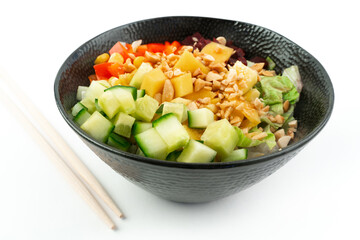 Vegetarian poke bowl in design black bowl with chopsticks below, isolated on white background. Green cucumber, red pepper, peanuts, corn, beetroot on top of sushi rice. Healthy vegetarian food.