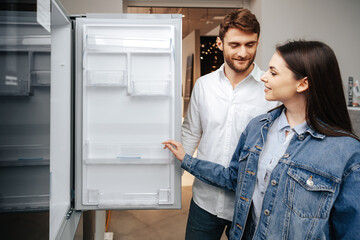 Young couple selecting new refrigerator in household appliance store