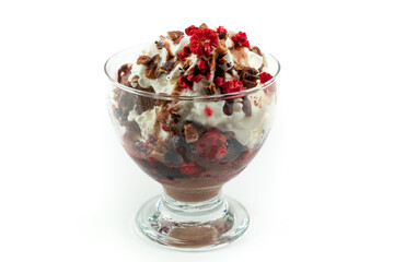 Chocolate ice cream with a cream, various nuts and frozen berries on top, in a glass cup, isolated on white background.