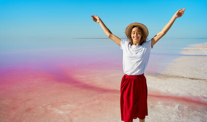 Tourist woman enjoying summer trip at pink lake, walking by salt flats with open arms
