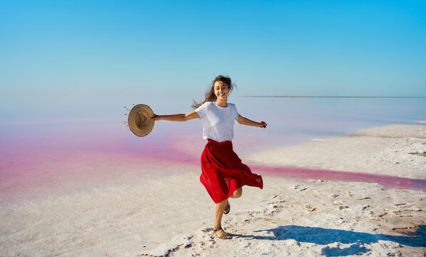 Happy smiling woman in red skirt dancing, dynamic moving at salt flats of pink lake