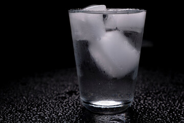 sparkling water, or vodka, tonic, or clear liquid in a glass of ice. on a black background with drops