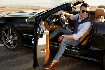 Handsome young man in luxury convertible car outdoors - obrazy, fototapety, plakaty