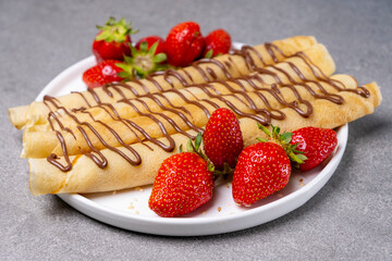 A plate of delicious pancakes or crepes roll with fresh berries, strawberries and chocolate on a concrete table. Top view, flat lay.