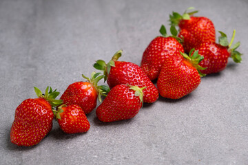 Composition of red ripe strawberries laid out in a row on a gray concrete background