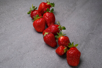Composition of red ripe strawberries laid out in a row on a gray concrete background