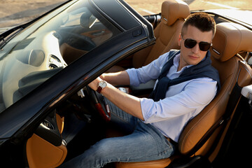 Handsome young man in luxury convertible car outdoors
