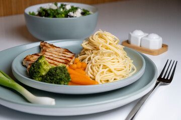 steak with spaghetti, pasta vegetables, baby carrots, and broccoli on a white plate.