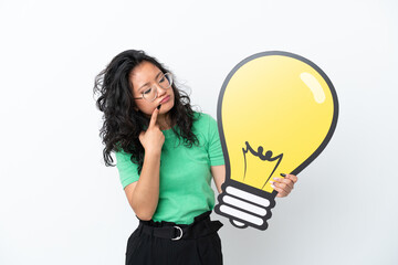 Young asian woman isolated on white background holding a bulb icon and having doubts