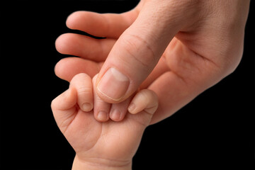 Father holding newborn baby's fingersnewborn . Hand of a newborn baby. Hands of parents and baby closeup. Black studio background. 