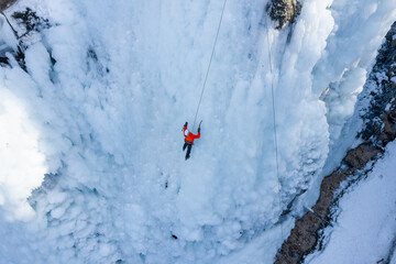 Man climbing on frozen waterfall by kicking with crampons into the ice and push up onto